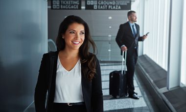 A woman in business attire walking through an airport, showcasing a professional look amidst travel hustle.