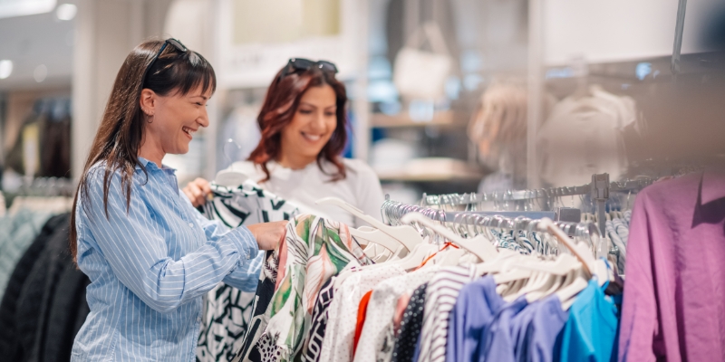 Two women examining clothing options in a retail store at Dania Pointe, close to Fort Lauderdale Airport.