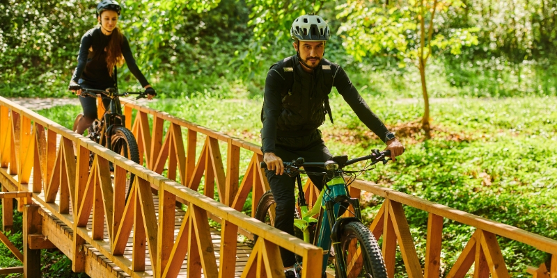 Two cyclists ride across a wooden bridge at Secret Woods Nature Center in Fort Lauderdale, enjoying the outdoors.