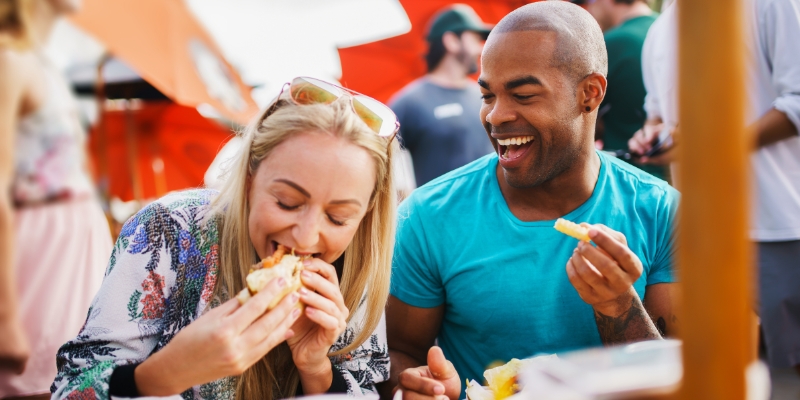 A man and woman savoring dishes at an outdoor food event during the Las Olas Wine & Food Festival in Fort Lauderdale.