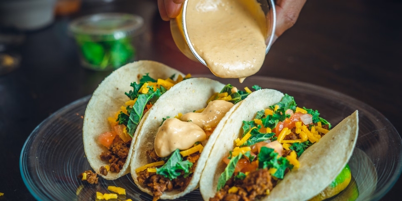 A person adds sauce to tacos, illustrating a tasty dish from the Fort Lauderdale Travel Guide focused on casual, budget-friendly dining.