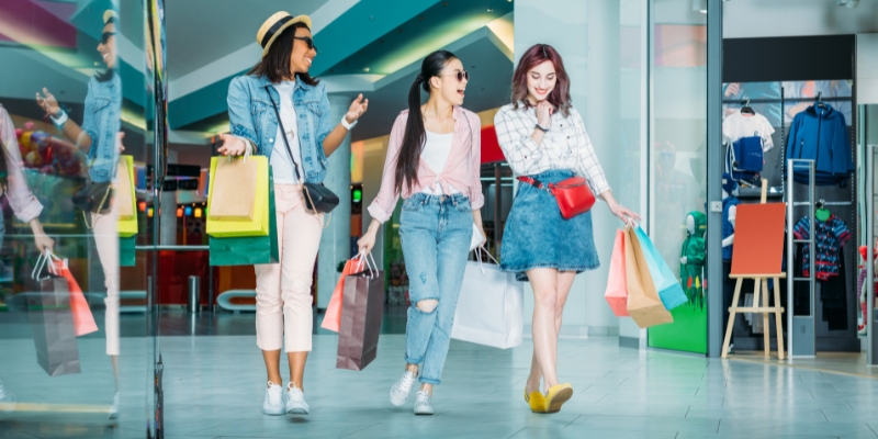 Three women with shopping bags navigate a mall, featured in the Dania Pointe Fort Lauderdale.