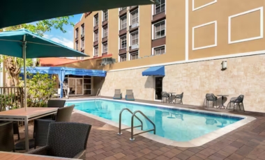 Outdoor pool and patio with chairs and umbrellas, providing a relaxing atmosphere at a hotel near Dania Pointe.