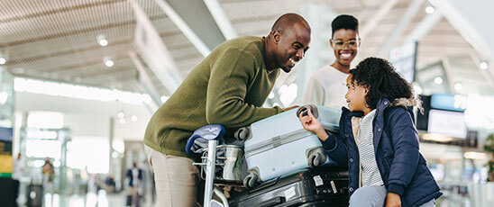 A family stands at the airport with luggage, ready for travel, promoting the Hampton Inn & Suites Fort Lauderdale's extended stay package.